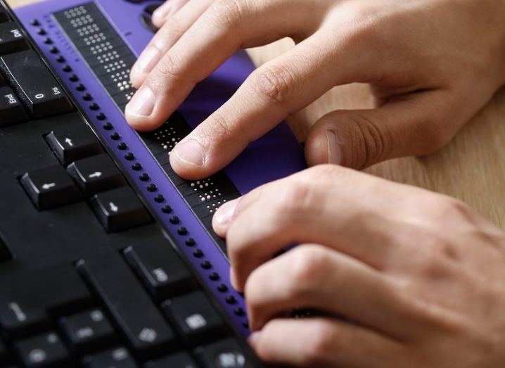 Hands using a braille computer display placed in front of a keyboard.