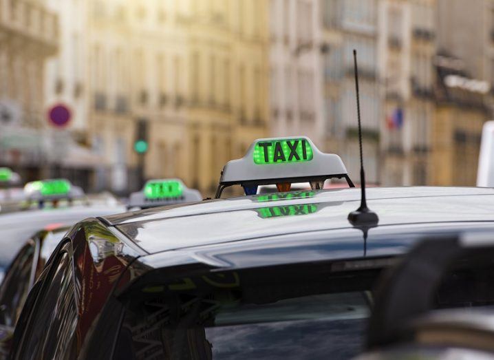Row of taxis in Paris with green lights on top of the cars.