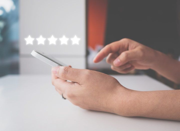 A woman using a smartphone to leave a five-star review of an online business.