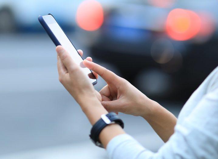 Woman's hands using a smartphone against a blurred city background.