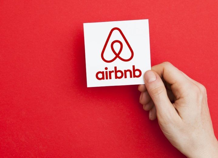 Hand holding a card with the Airbnb logo against a red background.