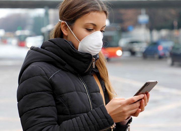 Woman wearing a face mask and looking at her phone on a street.