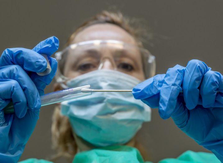 Woman wearing PPE while placing a coronavirus test swab into a test tube.