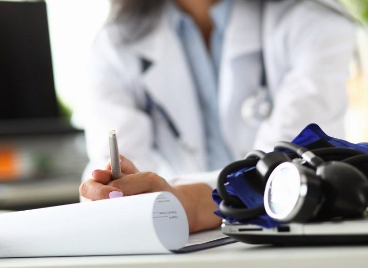 GP in a doctor's jacket with a pen and paper and stethoscope on the table.