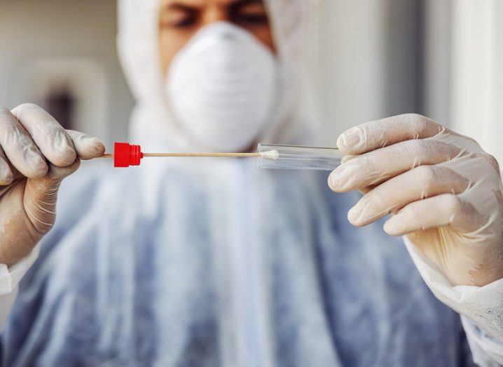 Man in PPE placing a swab in a test tube.