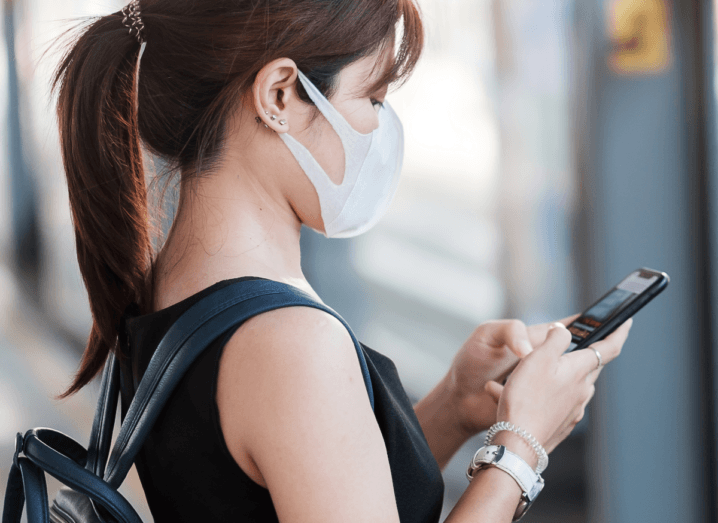 A woman wearing a mask using an iPhone X.