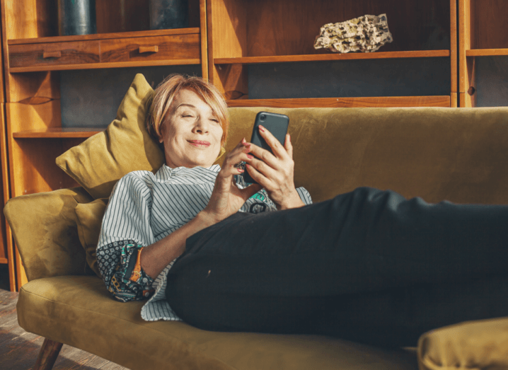 A woman lying on a sofa using a mobile phone and smiling.