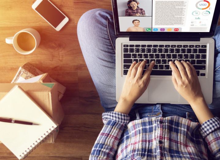 A bird’s eye shot of someone sitting cross-legged with a laptop on a Zoom meeting. There’s a notepad and coffee beside them.