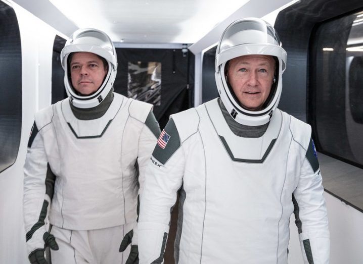NASA astronauts Bob Behnken and Doug Hurley in their SpaceX spacesuits walking down a white corridor.