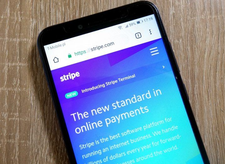 The Stripe website open on a smartphone screen against a wooden table background.