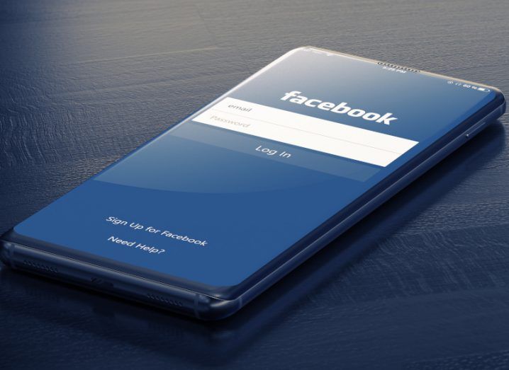 The Facebook loading page on a mobile, which is lying on a dark navy wooden surface.