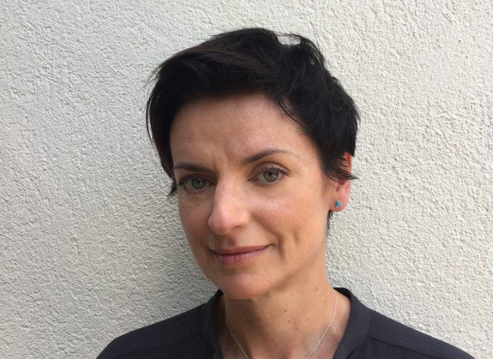 Headshot of a woman with short, dark hair against a whitewashed wall.