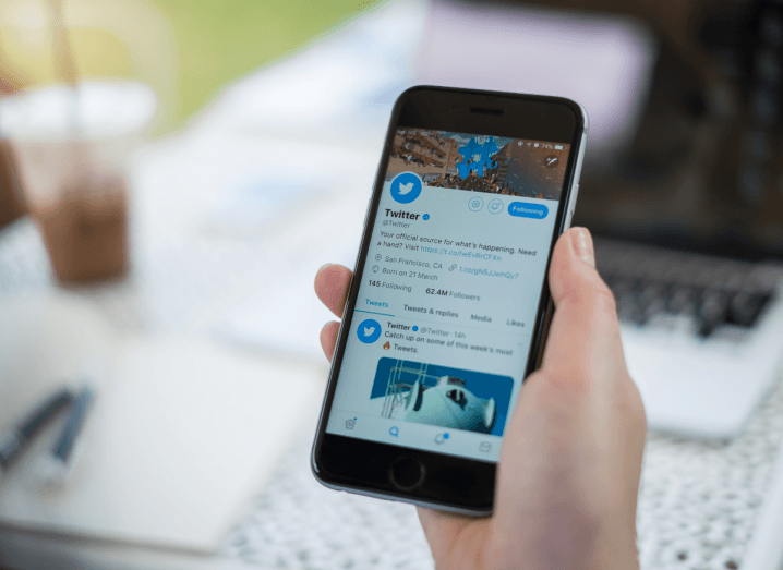 Twitter displayed on a smartphone in front of a laptop and an iced coffee.