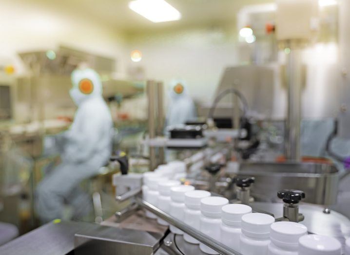 Medicine bottles on a production line with an employee wearing a full-body protective suit.