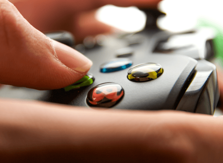 A close-up of an Xbox One controller with a person pressing their thumb on the A button.