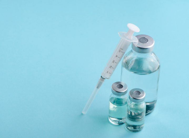 A syringe and three vaccine vials, one of which is much larger than the others.