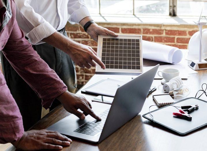 Pair of engineers at a table with a laptop, solar panel and small wind turbine on it.