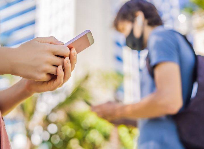 Two people holding their phones walking past each other on a city street.