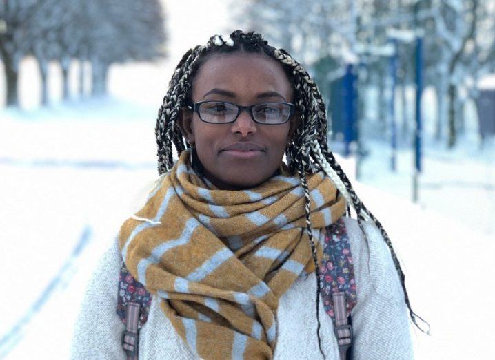 Abeba Birhane wearing a yellow scarf and white jacket against a snowy background.