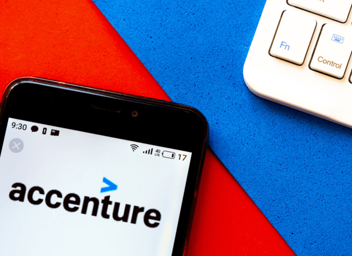 The Accenture logo displayed on a smartphone screen, beside the keyboard of a laptop.
