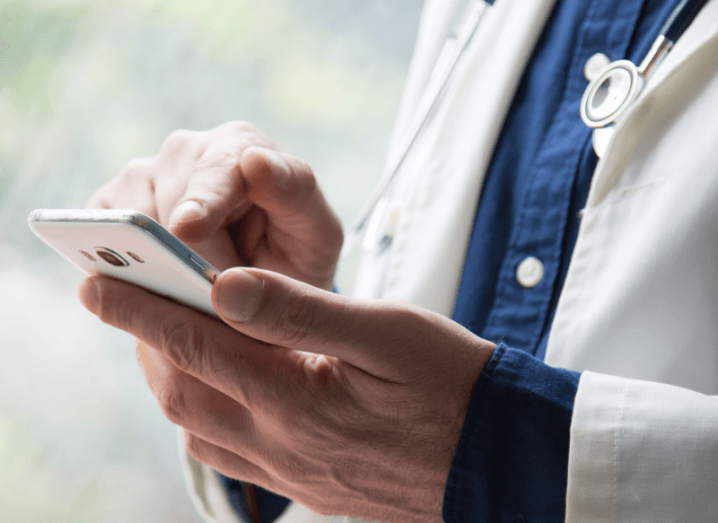 A doctor wearing a white coat using a smartphone.
