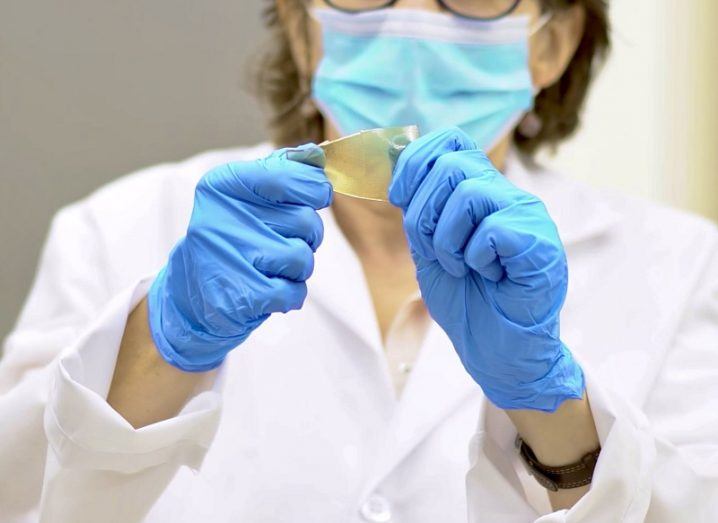 Scientist in full protective equipment holding the gold-coloured material up.