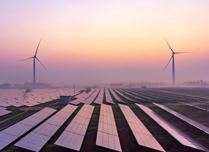 A solar farm and wind turbines at sunrise.