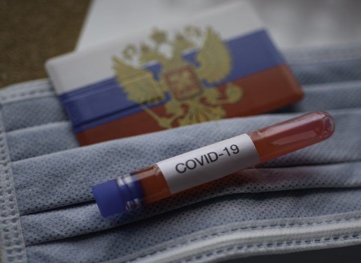 Test tube with Covid-19 written on it beside a Russian flag and face mask.