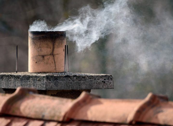 Chimney stack on a house roof releasing smoke.