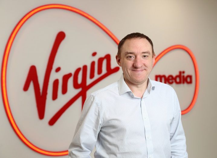 Paul Higgins smiling in a white shirt in front of a Virgin Media sign.