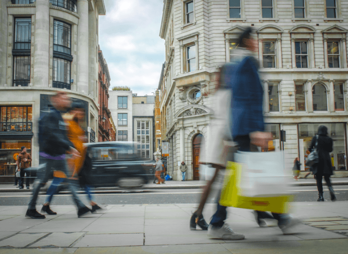 Busy pedestrians walking down a street carrying bags from retail stores.