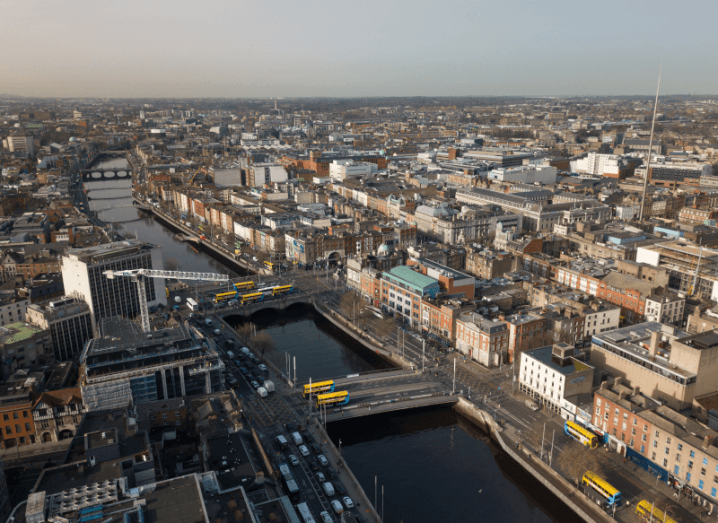 An aerial view of the Liffey river in Dublin city centre, with cranes above buildings and buses driving along the quays.