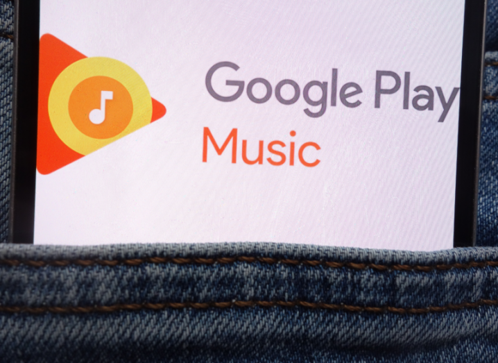 A smartphone in the pocket of denim jeans, displaying the Google Play Music logo on its screen.