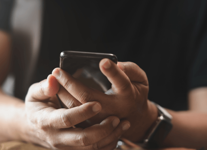 A person in a black T-shirt holding a smartphone.