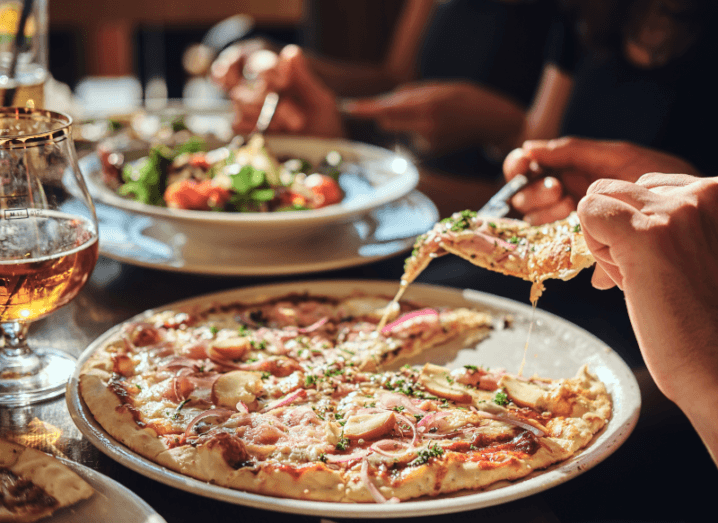 Two people eating a meal in a restaurant. There are plates with pizza and salad on the table and glasses of beer.