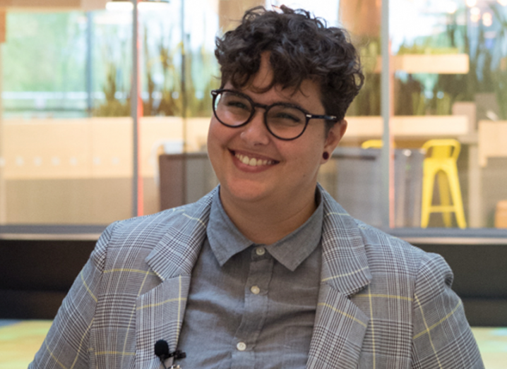 A woman with short brown hair and black-rimmed glasses wearing a grey plaid suit and a grey shirt.