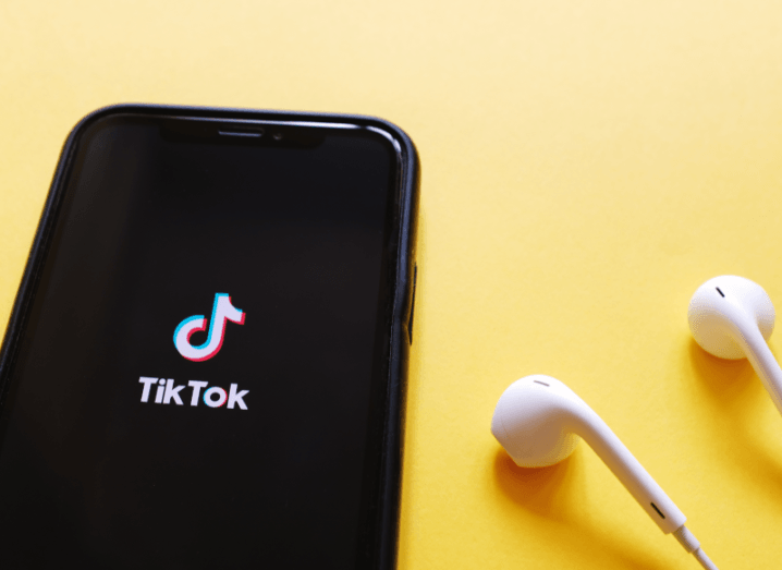 A phone displaying the TikTok logo on a yellow background, with white earphones beside it.