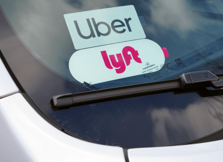 An Uber sticker and a Lyft sticker in a car window above the windshield wiper.