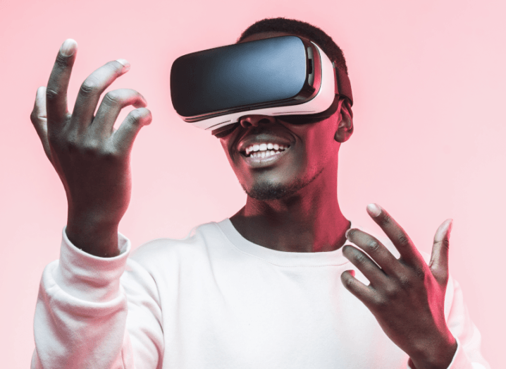A man wearing a VR headset in front of a pink background.
