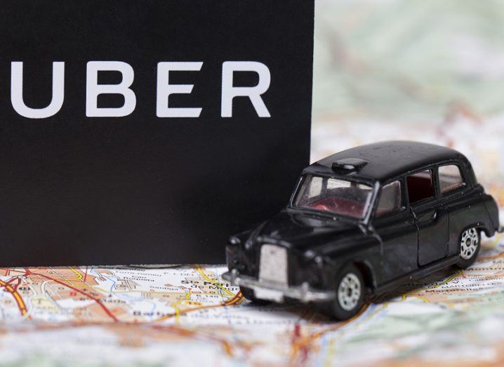 A black London taxi toy beside an Uber logo on a paper map.