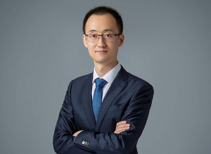 Tony Yangxu in a suit and tie crossing his arms against a grey background.