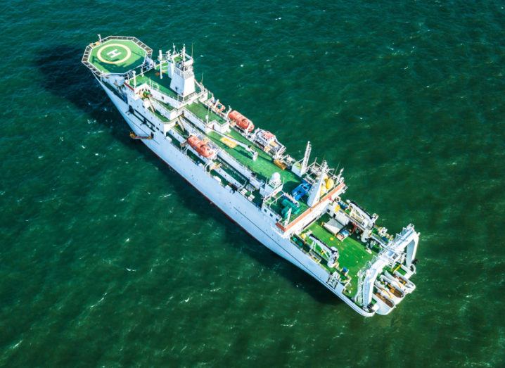 An aerial view of a large ship in the middle of the ocean, laying subsea cables.