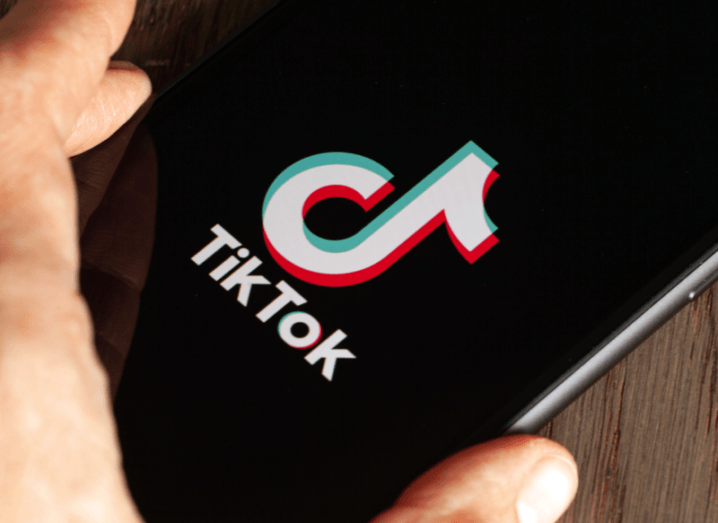 A person holding a smartphone with the TikTok logo on the screen.