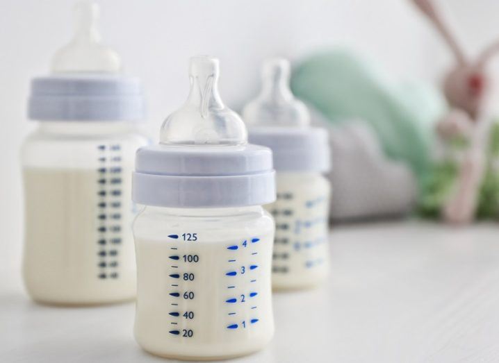 Three different sized infant-feeding bottles full of formula against a blurred background of children's toys.