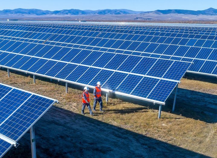 Two engineers wearing safety gear walking past a large-scale solar farm.