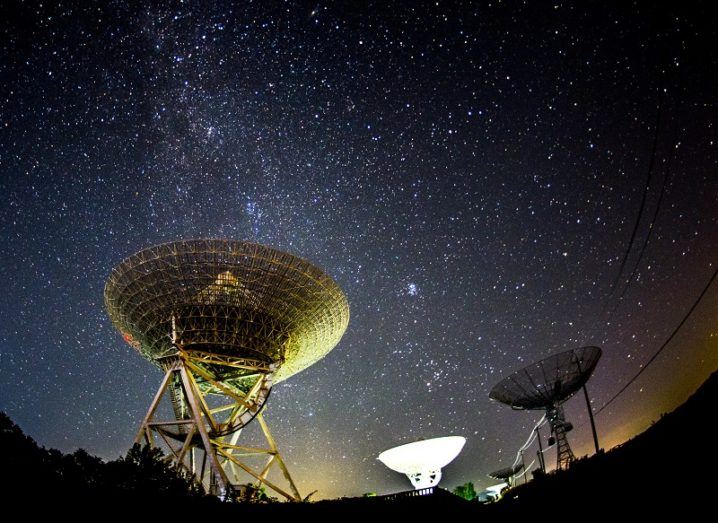 Fish-eye lens shot of three radio telescopes pointed to the night sky.