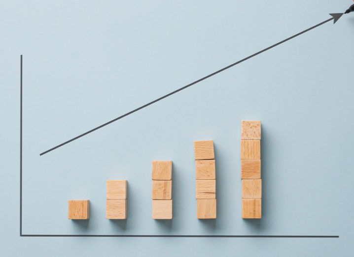 A bar graph made with wooden blocks against a blue background, with an arrow highlighting an upward trajectory.