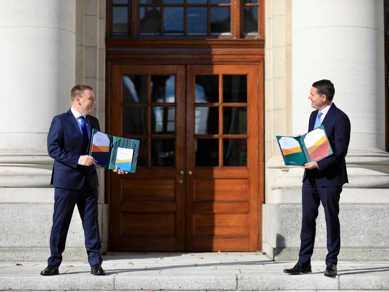 Two men in suits stand outside a large government building.
