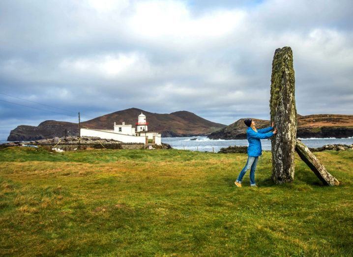 Woman touches an ancient stone near the Cromwell Point Lighthouse on Valentia Island, Co Kerry.