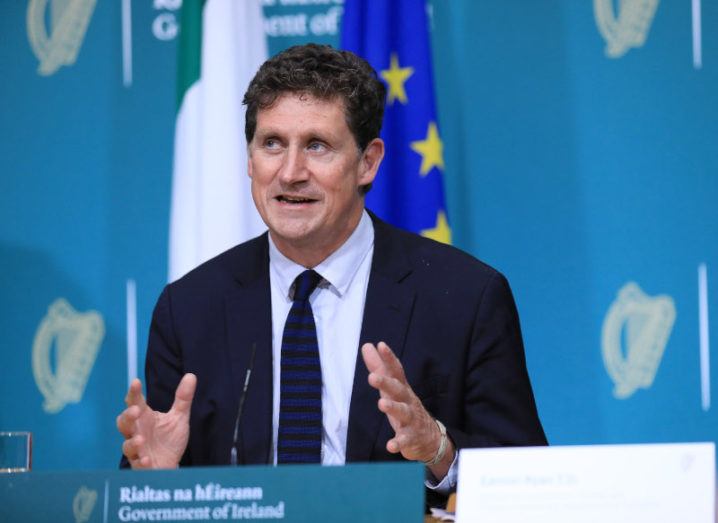 Eamon Ryan is wearing a suit and sits at a table during a government press conference.